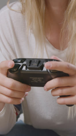 Vertical-Video-Close-Up-Of-Woman-With-Controller-Wearing-Headset-Sitting-On-Sofa-At-Home-Gaming-Online-